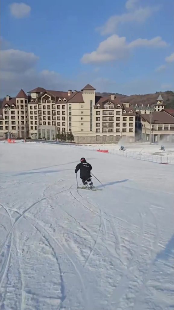 滑雪者在韓國雪場度假村建築前轉彎，介紹2026/2027韓國滑雪課程預約